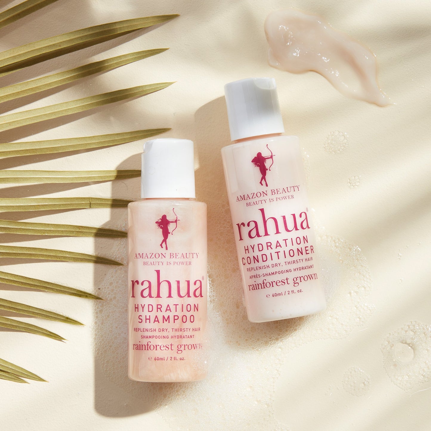 Two bottles of Rahua hydration shampoo and hydration conditioner on a textured beige surface with a leaf in the background|variant:2-oz
