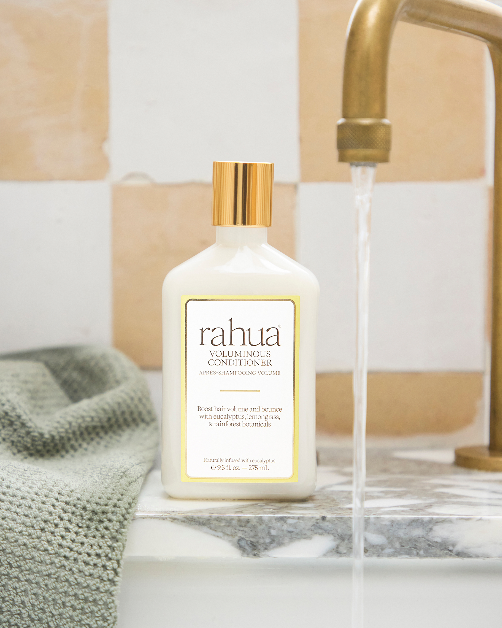 Bottle of Rahua conditioner on a bathroom counter with running water.|variant:93-oz,18-oz