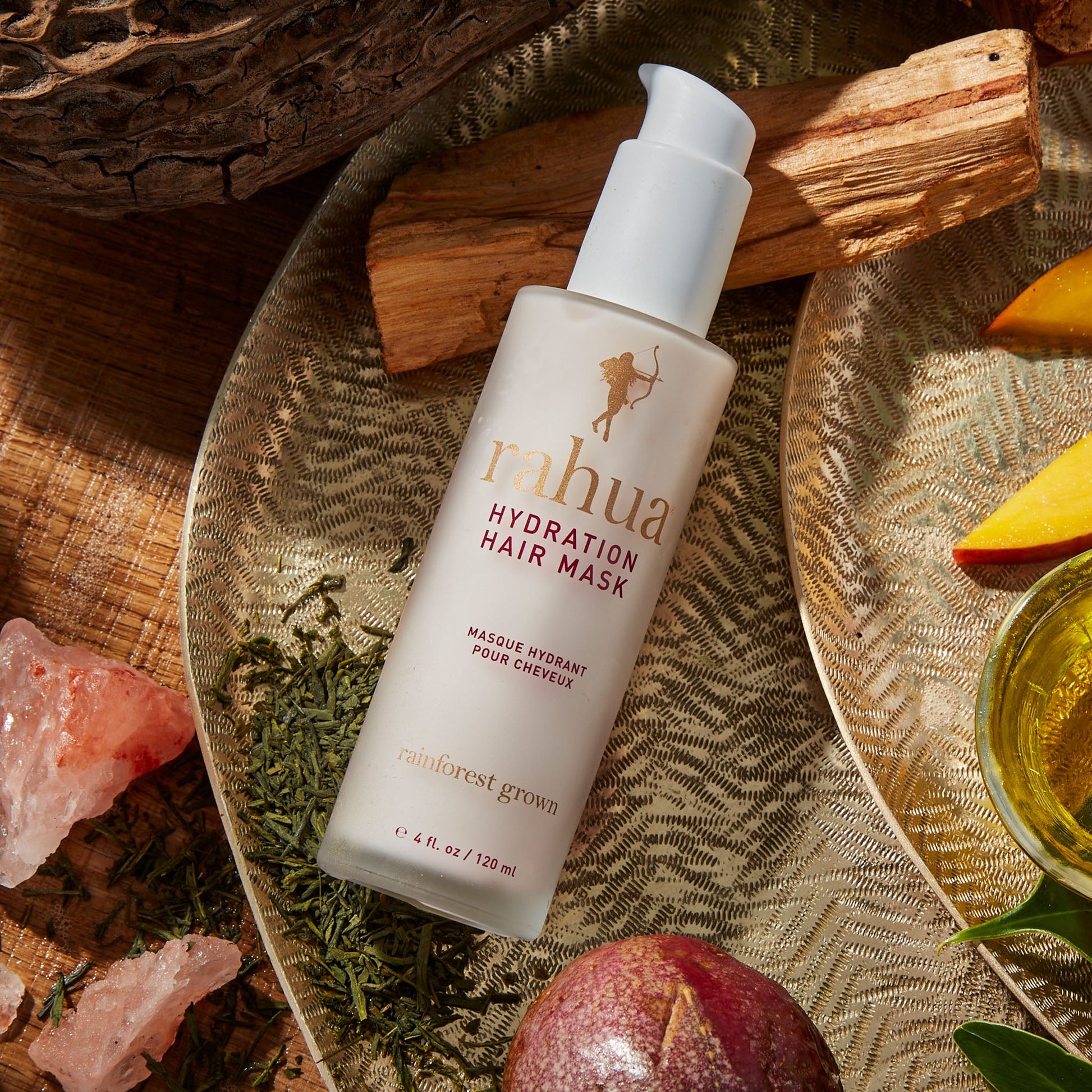 glass bottle of hydration hair mask on a golden plate resting on a wooden slab with passion fruit and mango in the background|variant:4-oz